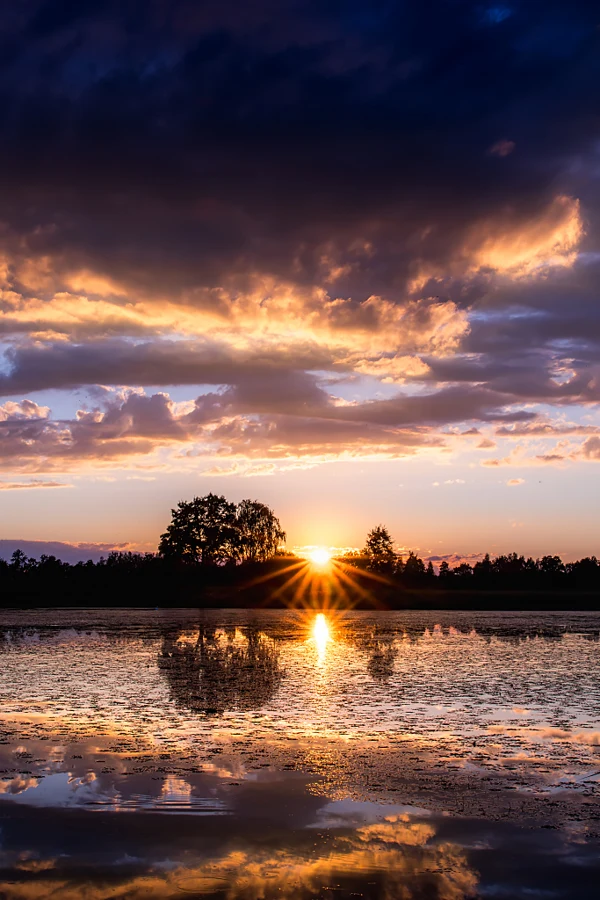 Słońce nad wodą pod barwnymi chmurami, kadr pionowy